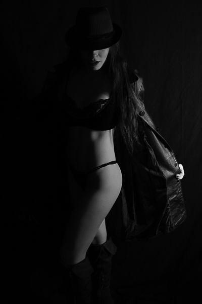 dramatic one light black and white. Woman wearing a fadora, leather coat, and black 2 piece lingerie